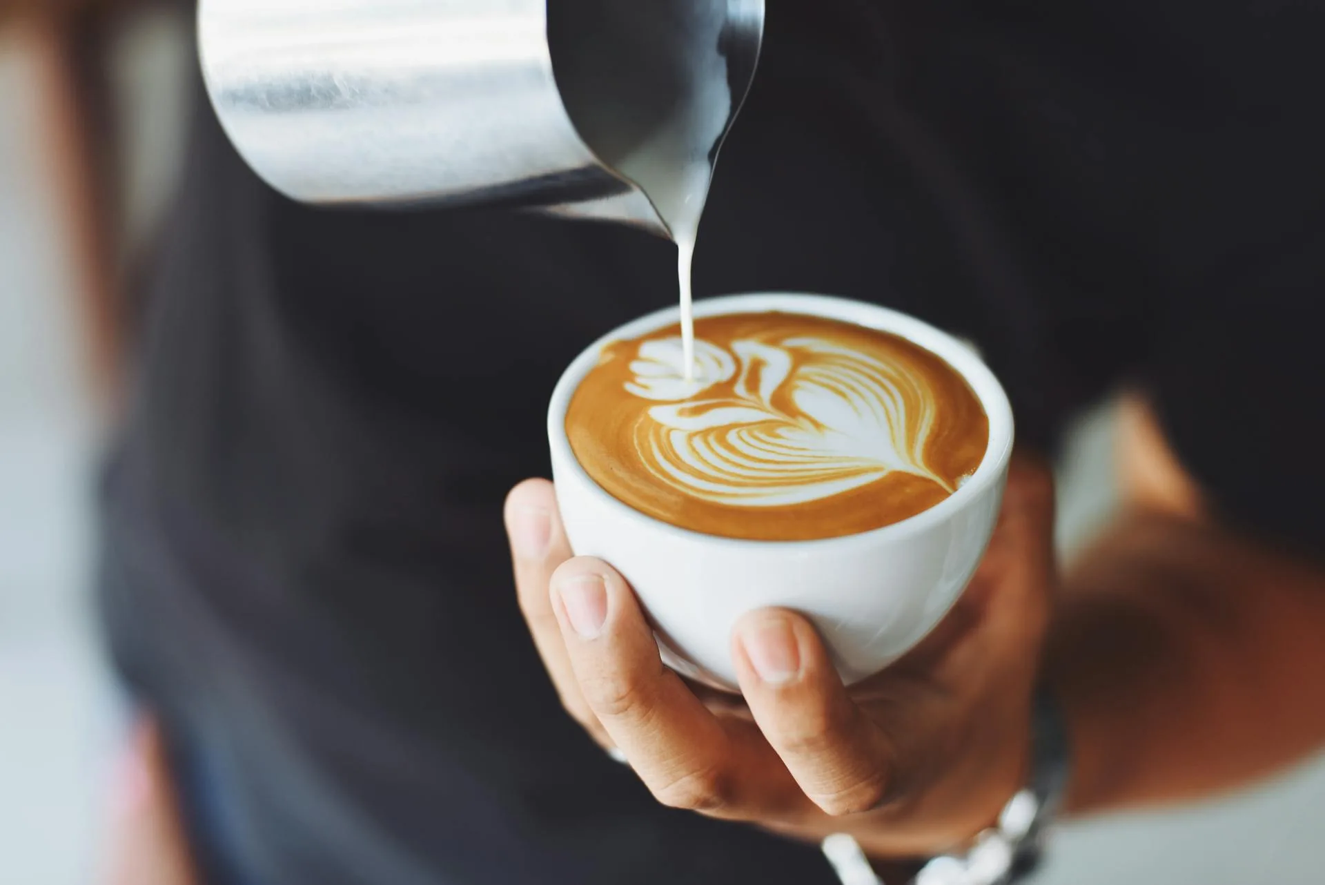 Professional barista pouring latte art into an espresso cup at an event